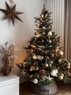 a decorated christmas tree with gold and silver ornaments in a basket next to a window