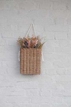 a wicker basket hanging on a white brick wall with dried flowers in the front