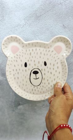 a hand holding a paper plate with a bear face on it, in front of a gray background