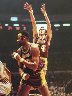 two men are playing basketball in front of an audience at a sporting event, one is reaching up for the ball