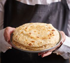 a person holding a plate with some food on it and wearing an apron in the background