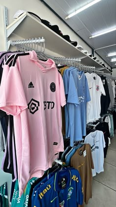 several soccer jerseys are hanging on racks in a store, with other shirts and shorts