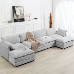 a living room with white walls and wood flooring has a large sectional couch in the middle