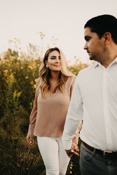 a man and woman holding hands walking through tall grass