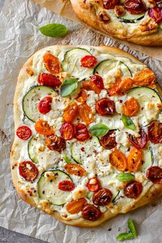 two pizzas with tomatoes, cucumbers and cheese on them sitting on paper