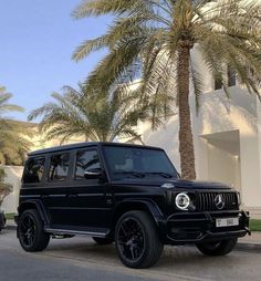 a black mercedes benz g class parked on the side of the road next to a palm tree