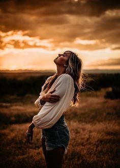 a woman standing in a field at sunset