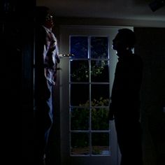 two people standing in front of a door at night with the light shining on them