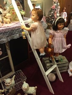 two dolls are standing on top of a ladder in front of a table full of stuffed animals