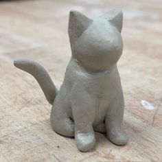 a small white ceramic cat sitting on top of a wooden table next to a mouse