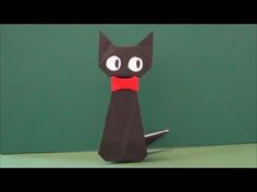 an origami cat with a red bow on it's neck sitting in front of a green wall