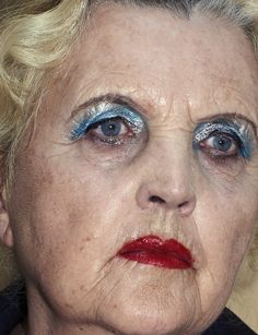 an older woman with blue and red eyeliners on her face is looking at the camera