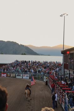 a man riding on the back of a brown horse in front of a large crowd