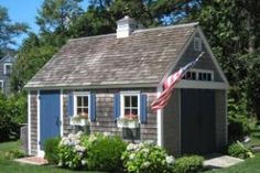 a small shed with an american flag on the roof and flowers in the window boxes