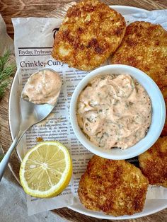 some fried food on a plate with a bowl of sauce and lemon wedges next to it