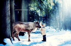 a little boy standing next to a cow in the snow near some trees and grass