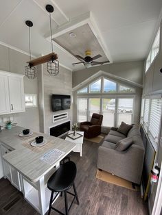 a living room and kitchen area in a mobile home with wood floors, white cabinets, gray couches, and ceiling fan