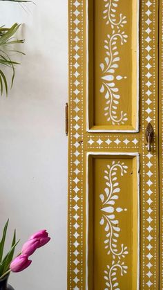 a yellow cabinet with white designs painted on the front and side doors, next to a potted plant