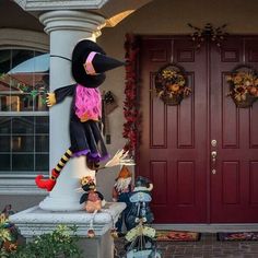 a large scarecrow statue sitting on top of a white pillar in front of a red door