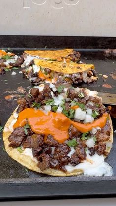 an uncooked pizza sitting on top of a black tray with cheese and other toppings