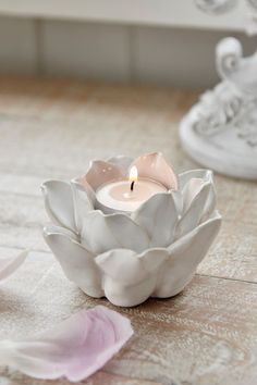 a candle that is sitting in a bowl on the floor next to some pink flowers