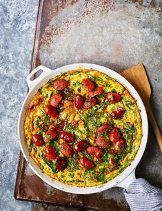 an omelet with tomatoes, spinach and cheese in a white dish on a wooden tray