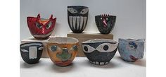 five different colored bowls sitting on top of a wooden block with faces painted on them