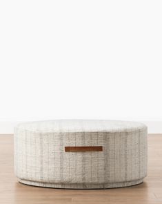 a round ottoman sitting on top of a hard wood floor next to a white wall