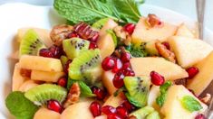 a white bowl filled with fruit and topped with nuts, kiwis, and pomegranate