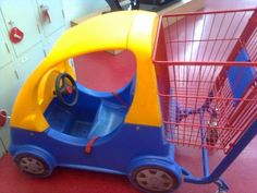 a blue and yellow toy car sitting next to a red shopping cart on the floor