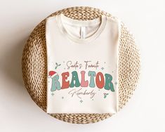 a white t - shirt with the words realtor printed on it sitting next to a wicker basket