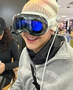 a young boy wearing goggles and smiling at the camera while another person works in the background