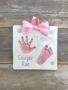 a ceramic plaque with pink handprints and a bow on it that says 1 months savyer rae