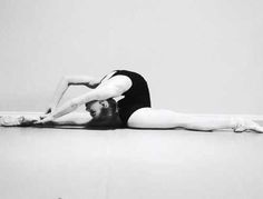 a woman in black leotard laying on the floor with her legs spread out