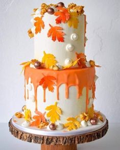 a three tiered cake decorated with leaves and acorns on a wooden stand