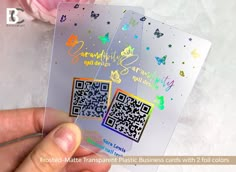 a person holding up two plastic business cards with qr code on them and flowers in the background