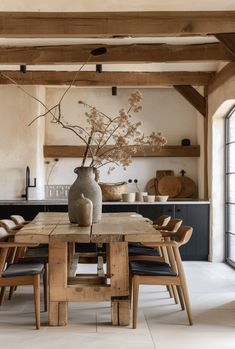 a vase with flowers on top of a wooden table in a room filled with chairs