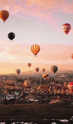 many hot air balloons are flying in the sky above some rocks and snow covered ground