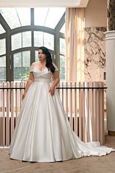 a woman in a white wedding dress standing next to a wall with large glass windows