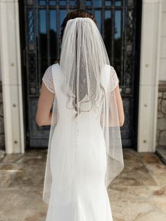 a woman in a white wedding dress and veil walking towards a church door with her back to the camera