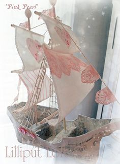 a pink and white sail boat is in a box with lace trimmings on it