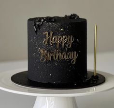 a black and gold happy birthday cake on a white plate with a toothpick