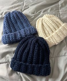 two knitted hats laying on top of a white bed next to eachother