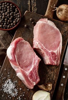 two raw pork chops on a cutting board next to garlic and peppercorst