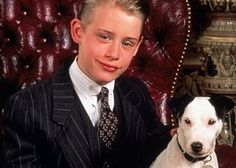 a boy in a suit and tie sitting next to a dog on a red chair