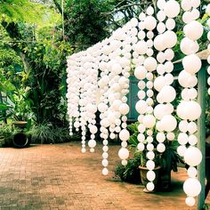 a bunch of white balls hanging from the side of a building in front of trees