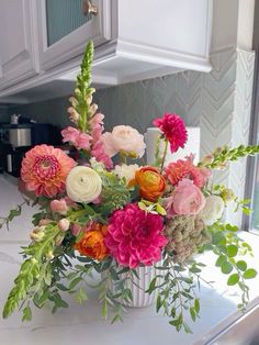 a vase filled with lots of colorful flowers on top of a kitchen counter next to a sink