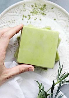 a hand holding a soap bar on top of a white plate next to a plant