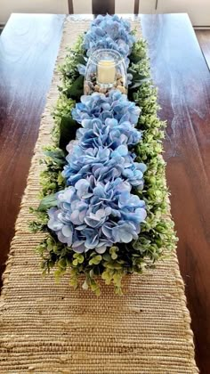 a table runner with blue flowers and greenery on the top is ready to be used as a centerpiece