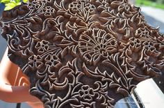 an intricately carved piece of wood sitting on the side of a road next to a potted plant